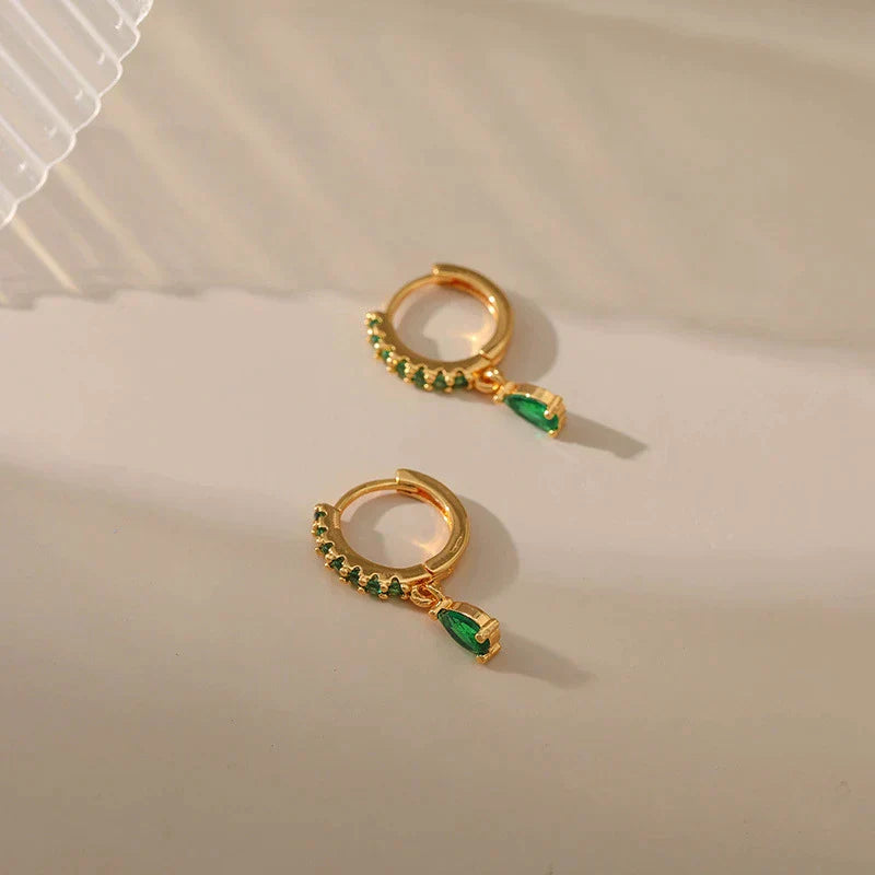 Brilhantes brincos dourados com zircônias cintilantes e uma encantadora esmeralda verde