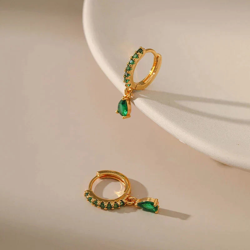 Brilhantes brincos dourados com zircônias cintilantes e uma encantadora esmeralda verde
